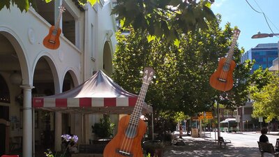 Photo of a building, pavement and gardens with ukeleles