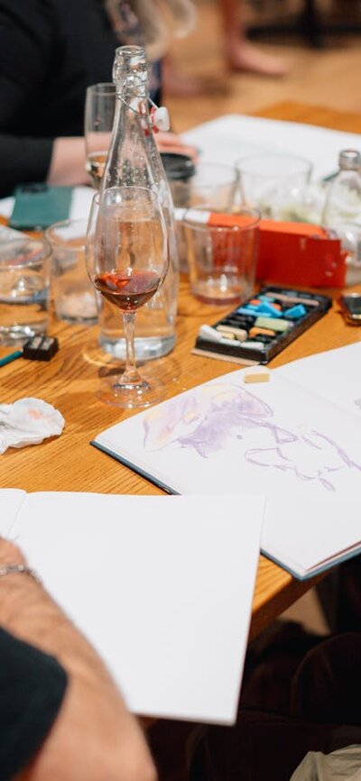 People sitting at a table drawing, with glasses of red wine