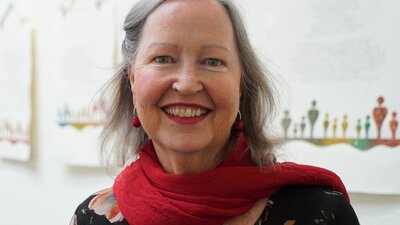 A smiling woman with gray hair wearing a red scarf over a dark floral top.