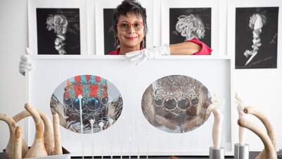 A portrait of artist Maria Fernando Cardoso in her studio posing with photograph of maratus spiders