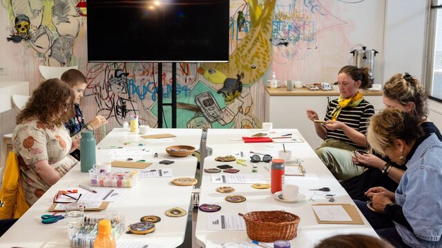 Workshop participants engaged in hands-on craft activities around a table in an art-filled studio.