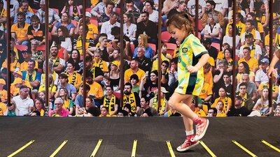 Matildas: Make and Move at the National Portrait Gallery A child wearing a Matildas jersey jumps on an indoor soccer footwork activity.