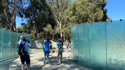 People examine a memorial to service nurses. People flanked by the glass walls of the Australian Service Nurses memorial.