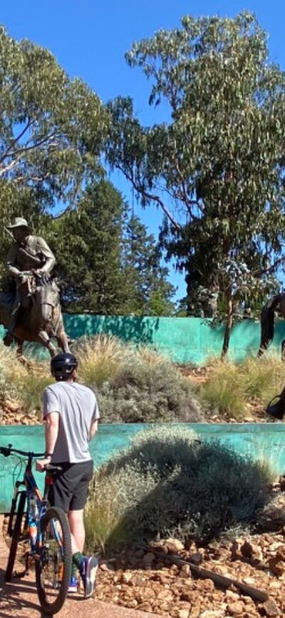 People at the Boer War memorial. People on bikes at the Boer War memorial, which features sculptures of large humans on large horses.