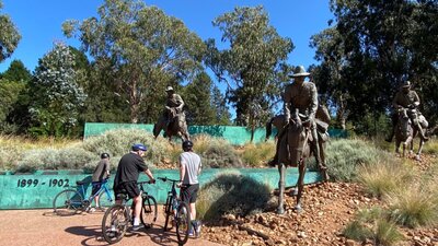People at the Boer War memorial. People on bikes at the Boer War memorial, which features sculptures of large humans on large horses.