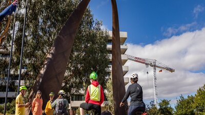 The New Zealand Memorial people on bikes beneath the giant handle of the New Zealand memorial