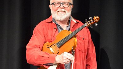 Old man with glasses wearing a red jacket whiling and holding a viola