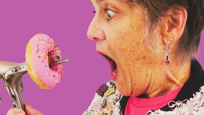 Anyone want a donut? Woman dressed in silver sparkly jacket holding a speculum which is holding a donut