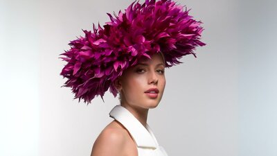 The photograph depicts a model wearing a unique pink headwear piece similar to a flower blooming.