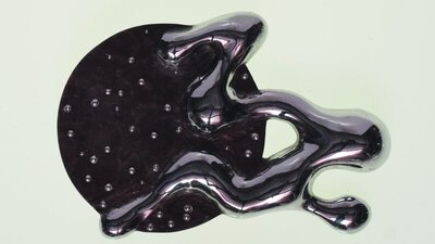 A shiny black abstract jewellery piece, combining a circle, squiggle and gems