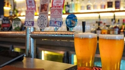 Two beers sitting on a bar in front of the bar taps