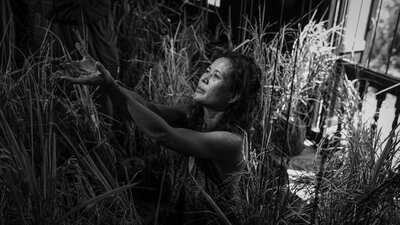 Black and white image of woman reaching hands up to left of image with grass in background