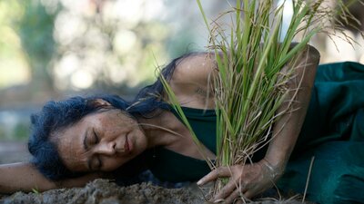dark haired woman lying on soil holding grass
