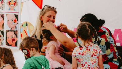 Children getting their facepainted whilst a smiling woman watches on