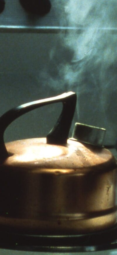 Photo of a kettle boiling on a stovetop and a teacup on the counter