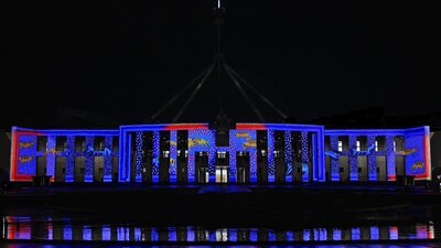 Parliament House at night, illuminated in blue & red light with projected artwork across the façade