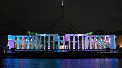 Parliament House at night time with the front facade lit up with the Honey Ant artwork.