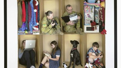 Moving Again - A Military Family by Rebecca Polonski moving boxes with objects in them and family members sitting in some of the boxes