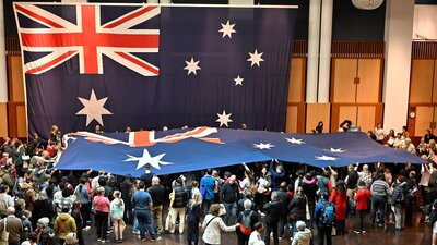 Visitors hold a giant Australian flag beneath a large Australian flag in Parliament House.