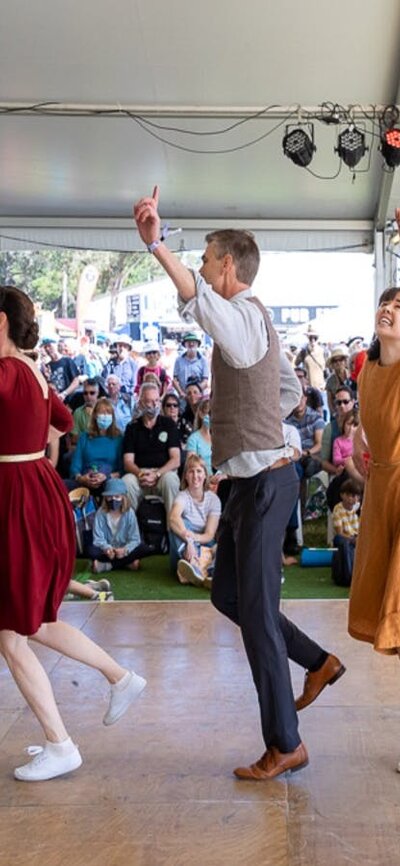 7 people dressed in bring colours perform a dance for a crowd