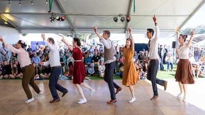 7 people dressed in bring colours perform a dance for a crowd