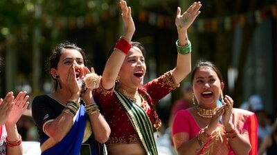 Three women in cultural dress clap for the festival parade performers