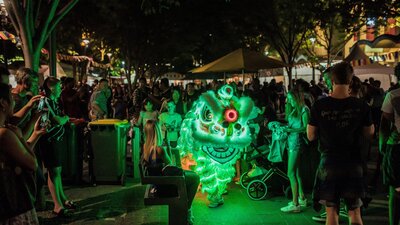 Lion dancer lit up in green walks through the festival crowd