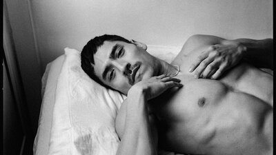 Luke Austin 'Aitor' 2025 (detail). National Photographic Portrait Prize 2026 Finalist © Luke Austin A monochrome pigment photographic portrait of a shirtless man laying on a bed, looking at the camera