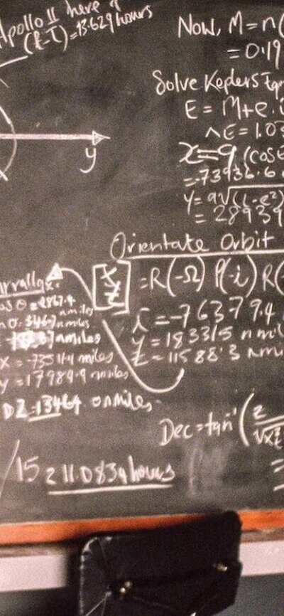 Two men stand with a blackboard with calculations on it