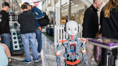 Small robot in the foreground and people looking at other displays in the back