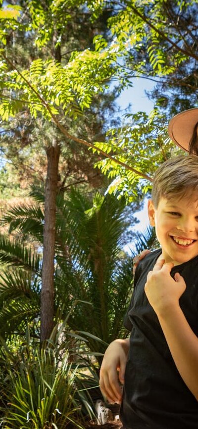 A mother and two children smile in awe at the size of the animatronic T-Rex  in lush fern gardens.