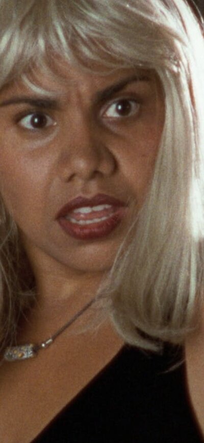 NFSA Restores: Radiance Woman looks surprised wearing a blonde wig and red lipstick