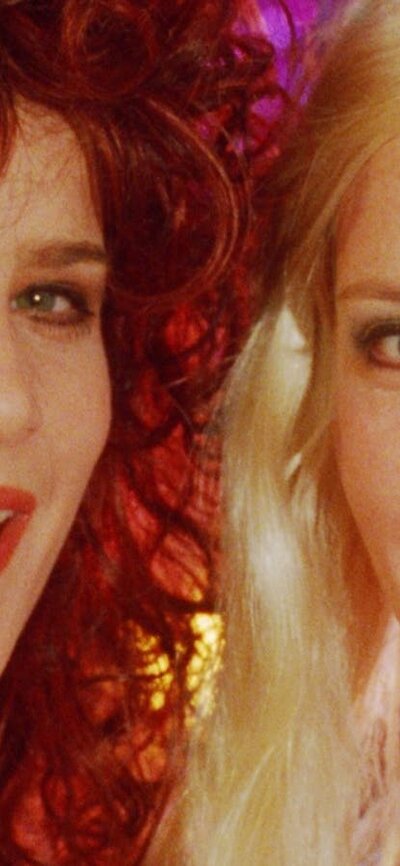 NFSA Restores: Muriel's Wedding Two women look directly at the camera midway through song, woman on left with big curly hair