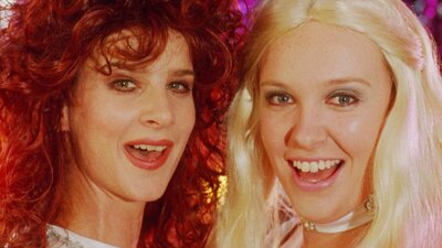 NFSA Restores: Muriel's Wedding Two women look directly at the camera midway through song, woman on left with big curly hair