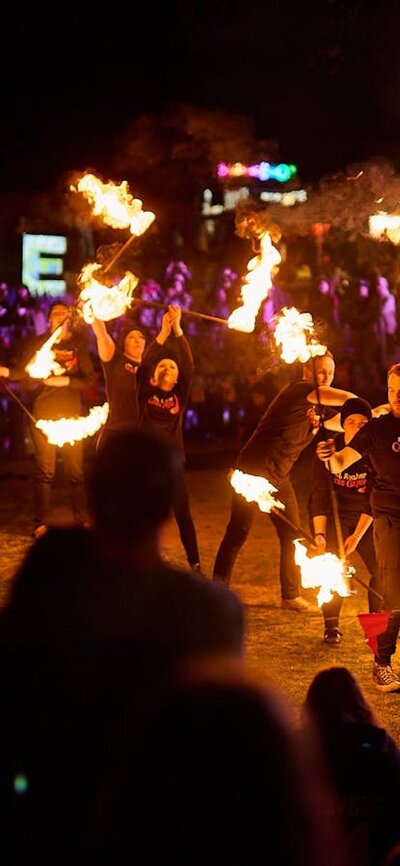 Fire performers entertain a crowd at night with flames, with lit “FLORIADE” sign behind.