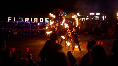 Fire performers entertain a crowd at night with flames, with lit “FLORIADE” sign behind.