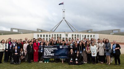 Large group of people in front of Australian Parliament House with a conference banner