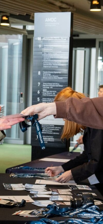 Two attendees collecting their conference lanyards from staff at a registration table