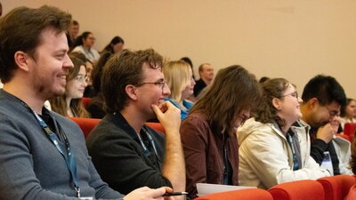 A row of conference attendees, two attendees are seen smiling in the foreground
