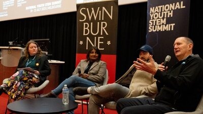 Four members of a discussion panel sitting on chairs, person in the foreground speaking with mic