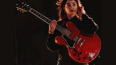 Photo of the artist, Olivia Ubergang A lady stands on stage holding a red guitar