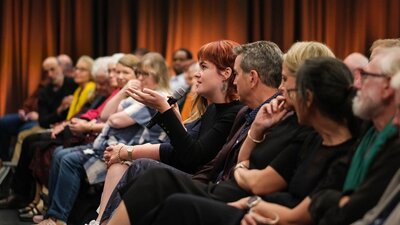 A person is sitting in an audience holding a microphone