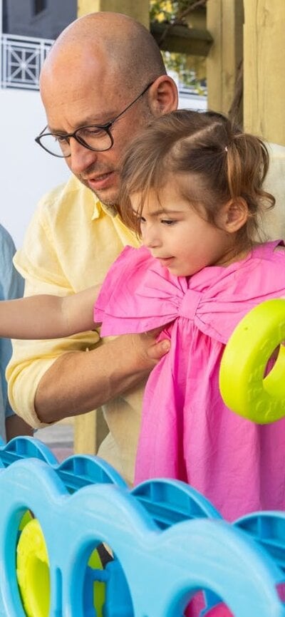 A father holding his young daughter while she places hoops into an oversized Tick-tack-toe game.