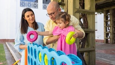 A father holding his young daughter while she places hoops into an oversized Tick-tack-toe game.