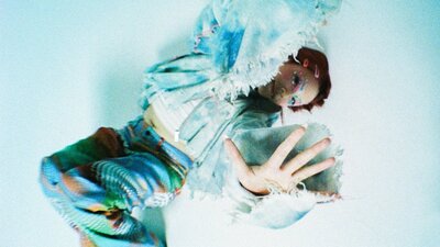 YURA, Korean Australian singer-songwriter, 2022. Photo: Cal Foster Performer posing on ground with her hand up to camera