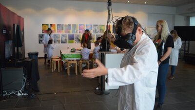 A boy wears a virtual reality headset and a white lab coat.