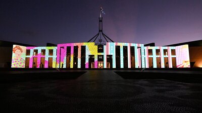The Parliament House façade illuminated in bright colours.