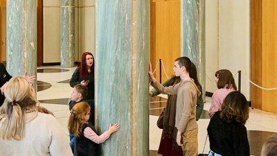 Tour participants in the Marble Foyer of Parliament House interact with one of the marble pillars