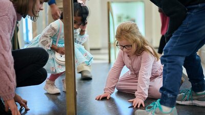 Children gather around to look at the Marble Foyer floor and a fossil within the marble floor