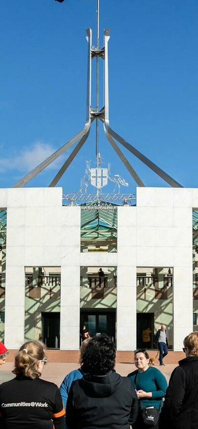 Tour group stands outside Parliament House on the Forecourt Mosaic listening to a tour guide